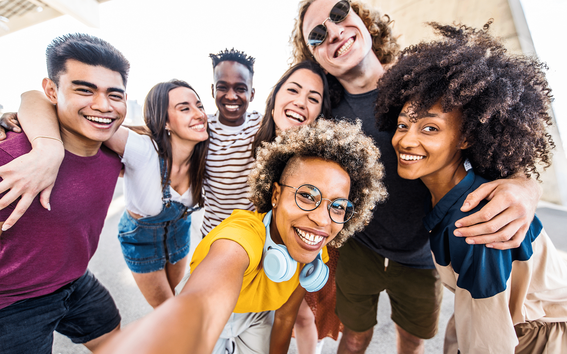Photo of a diverse group of teenagers with their arms around one another crowding in for a group selfie.