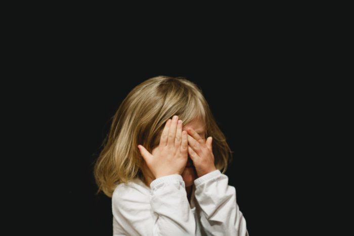 child surrounded by a black background and covering their face