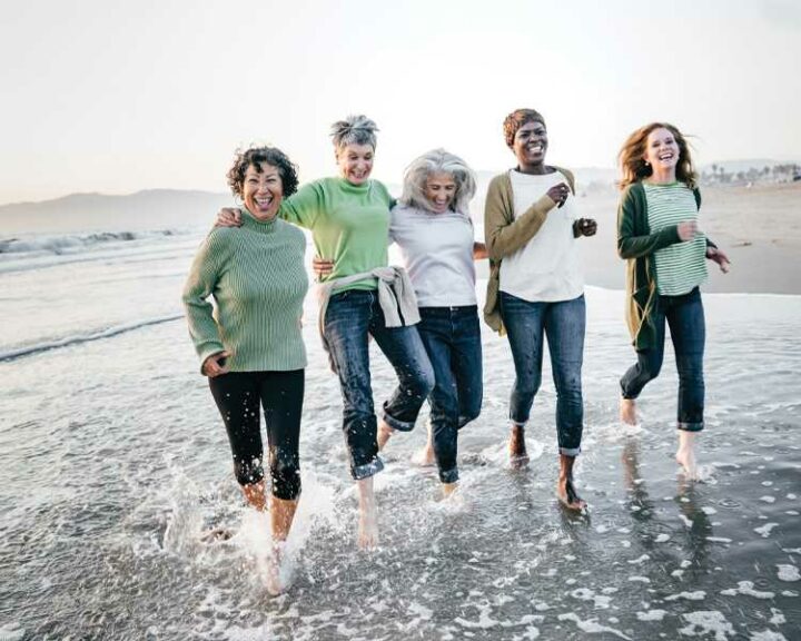 Five women laughing and kicking the water on the beach