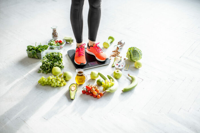 Sports woman weighing with healthy food around