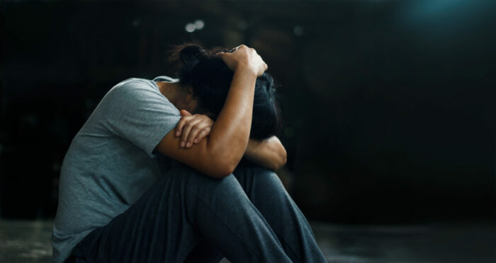 A depressed woman is sitting alone on the floor in a dark room