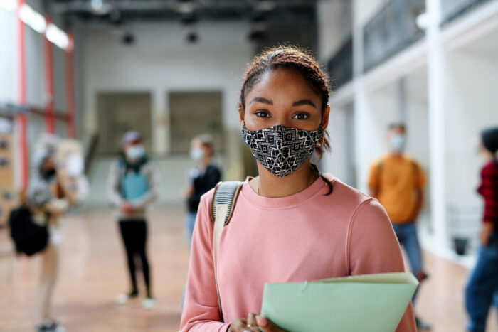 African-american student with a face mask on, carrying folders while back at school