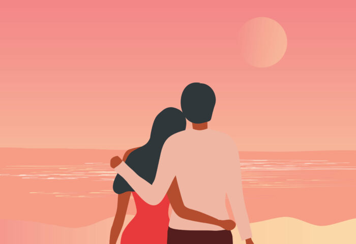 Loving couple embracing and looking at the moon on the beach against a sunset sky