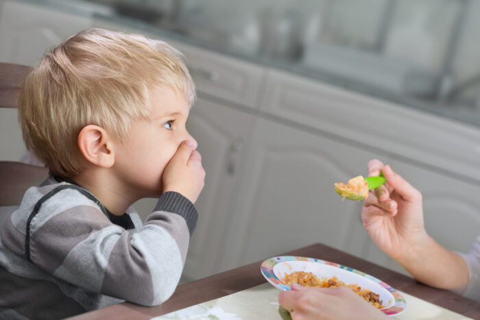 Blond boy holds hand on his mouth to stop eating