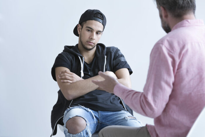 Teenager with a serious expression in deep in though with their arms crossed and sitting in a chair while someone talks to them