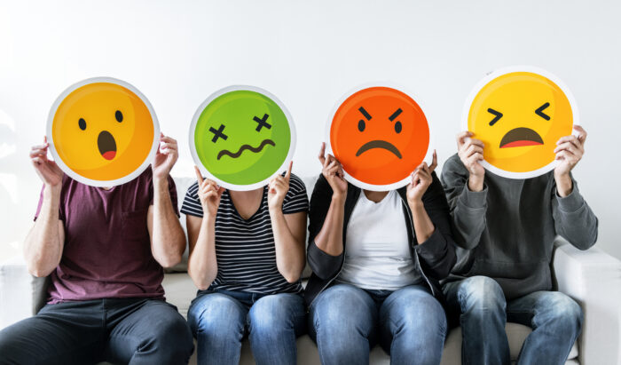 4 people holding emoticons faces that have different emotions on them