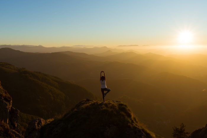 person standing on the mountain doing a yoga pose while overlooking the sunset