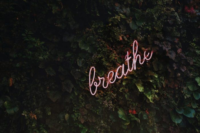 pink breathe sign written in cursive is against leaves