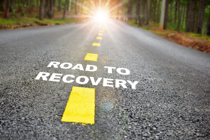 Road to recovery written on a gravel road that's in the direction of a sunbeam