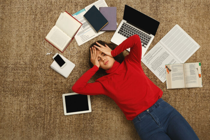 Tired student girl lying on the floor with books, a laptop, and ipad