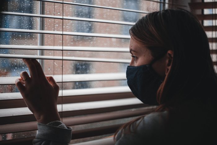 teen girl looking out rainy window with mask on