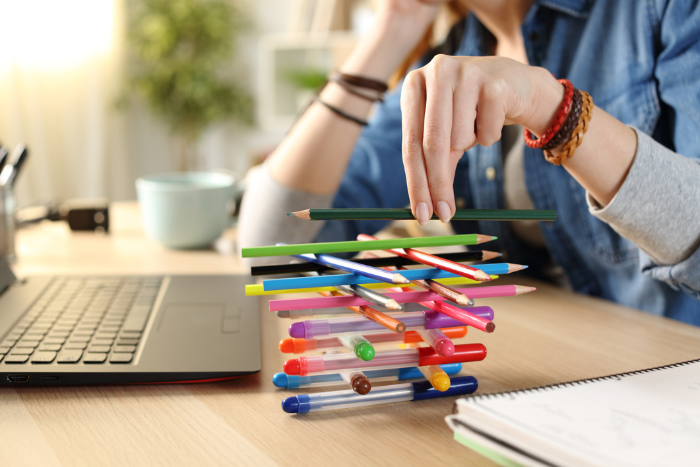 Person stacking pencils and pens on a table next to a laptop